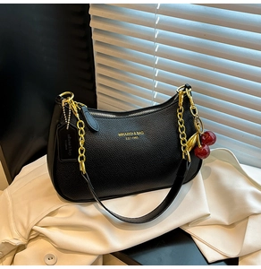 Gros plan d'un sac à main en cuir noir avec chaîne dorée et pendentif cerise rouge