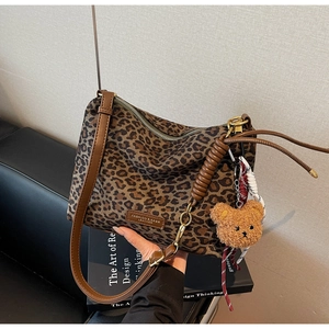Detailed close-up of leopard print tote bag with brown leather strap and plush bear charm