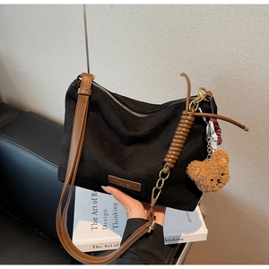 Détail du sac cabas en cuir noir mat avec bandoulière marron et breloque ours en peluche