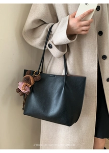 Detail view of black litchi grain tote bag with shoulder strap and plush bear charm