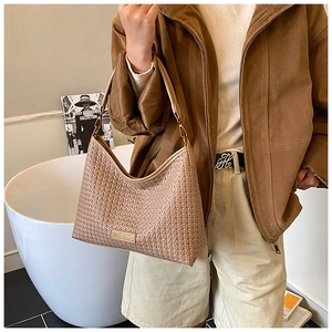 Close-up of earth-tone woven shoulder bag with detailed texture and golden metal logo plate