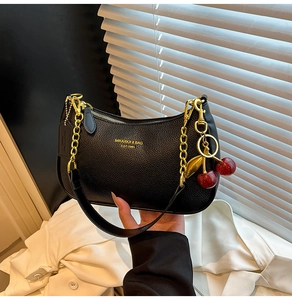 Detail of black lychee leather crescent bag with gold chain and cherry charm