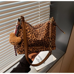 Detail of leopard print tote bag featuring a plush bear charm and brown leather strap