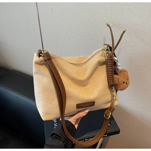Détail du sac cabas en daim avec écusson en cuir et breloque décorative en ours en peluche