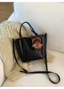 Detail of black litchi grain bucket bag on a sofa with a cute plush bear charm