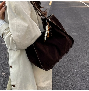 Detail of a deep brown suede tote bag with colorful wooden beads on a light coat