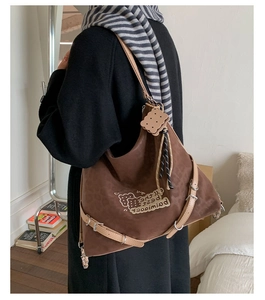 Detail of dark brown suede tote bag with embroidery, buckle straps and biscuit charm
