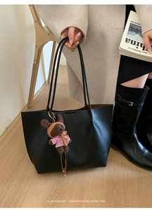 Close-up of black pebble leather tote bag with a cute plush bear charm decoration