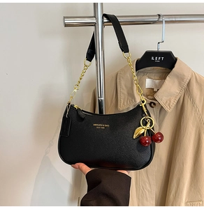 Detail of black lychee grain leather crescent bag with golden chain and cherry charm