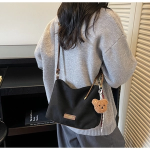 Détail du sac cabas noir avec étiquette en cuir, breloque ours et écharpe rayée