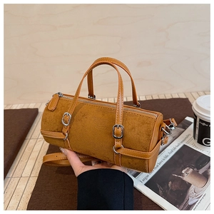 Close-up of brown suede cylinder bag with leather trim and metal buckle on wood