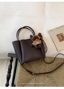 Detail of dark brown pebble leather bucket bag with a cute striped teddy bear charm
