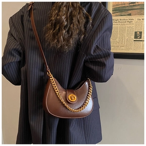 Sac croissant marron foncé avec chaîne dorée porté par un mannequin en mode street style