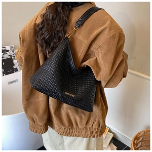 Close-up of black woven shoulder bag with golden metal hooks and wide strap worn by a model