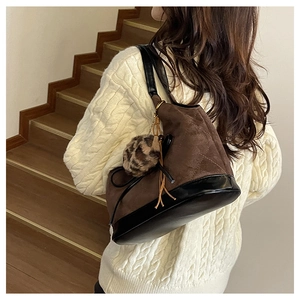 Close-up of brown suede bucket bag with black leather straps and leopard fur ball charm