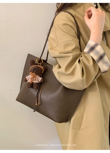 Detail of dark brown pebble leather tote bag with teddy bear charm and trench coat styling