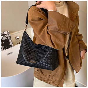 Close-up of black woven hobo bag with gold hardware and logo on brown suede coat