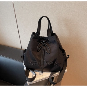 Detail of black nylon bucket bag featuring YOU I BEAR embroidery and drawstring closure