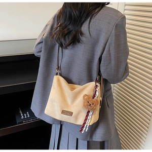 Détail d'un sac hobo en daim beige avec logo en cuir marron et breloque ours en peluche