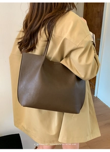 Rear view of model wearing a minimalist dark brown textured leather tote bag in warm indoor light