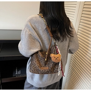 Chic leopard print tote bag with plush bear charm and plaid scarf detail on a model