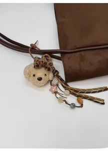 Close-up of a plush puppy charm with a leopard bow and beaded rope on a brown tote bag