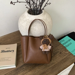 Close-up of brown pebbled leather bucket bag with cute hand-knitted bear charm