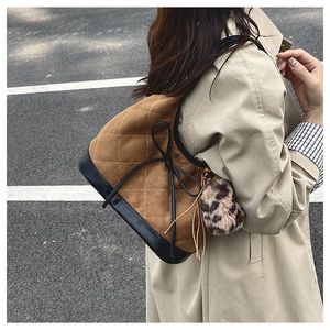 Detailed view of brown suede shoulder bag with beige stitching and leopard pompom charm