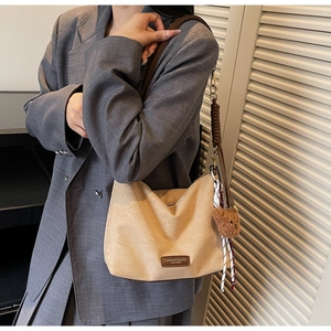 Gros plan du cabas en daim beige avec étiquette en cuir et breloque ours sur modèle