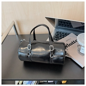 Close-up of black glossy leather barrel bag with silver buckle details and top handle