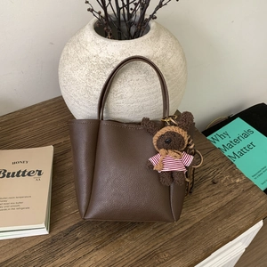 Macro detail of dark brown lychee grain leather handbag with cute bear charm and top handle