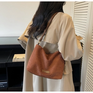 Détail du sac cabas en daim marron avec bandoulière réglable et plaque de marque en métal