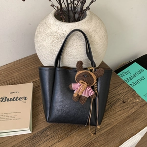 Chic black litchi grain leather bucket bag with a cute teddy bear charm on wood table