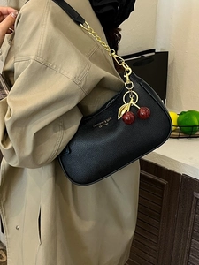 Black underarm dumpling bag with gold chain and red cherry charm on trench coat