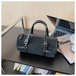 Detail of black cylindrical suede handbag featuring leather strap and silver metal buckle