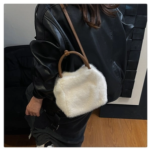 Close-up of white plush crossbody bag with brown leather handles worn with a leather jacket