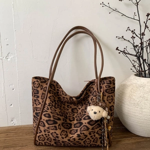 Detail view of leopard print tote bag with plush bear charm on rustic wooden table