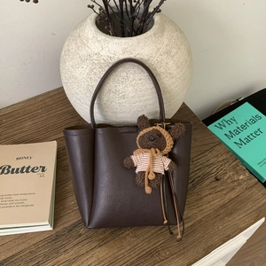 Detail of dark brown lychee leather bucket bag with a cute plush bear pendant accessory