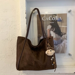 Close-up of brown frosted faux suede tote bag with plush bear charm and beaded tassel detail
