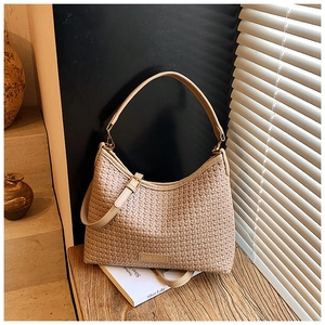 Detail of beige woven texture shoulder bag with brand logo tag on a wooden surface
