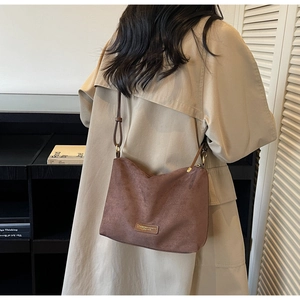 Détail du sac cabas en daim marron avec écusson en cuir et fine bandoulière élégante