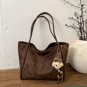 Detail of deep brown frosted suede tote bag with a cute puppy plush charm on a wooden table