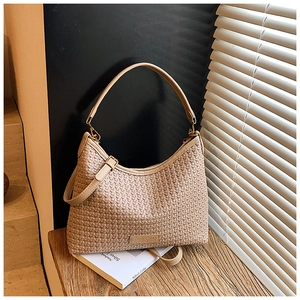 Macro shot of beige woven hobo bag showing detailed texture and gold hardware on wood