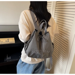 Grey nylon drawstring backpack with YOUJIBEAR embroidery shown on a model in daily use
