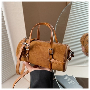 Detail of a brown suede cylinder bag showing leather handles and metal buckle accents