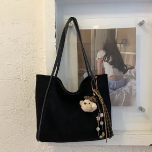 Detail of a black faux suede tote bag with a plush bear charm and beaded ornament