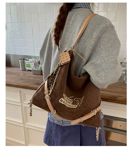 Close-up of brown suede tote bag featuring adjustable leather straps and cookie motif