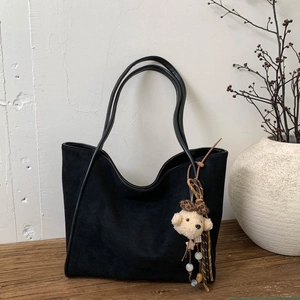 Close-up of black matte tote bag featuring leopard bow teddy bear charm on wood surface