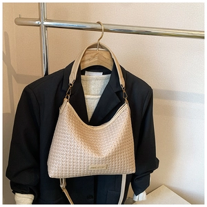 Detail view of beige woven hobo bag with leather handle and metal logo on a blazer
