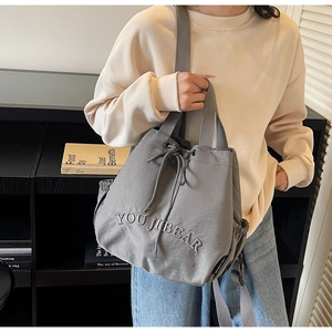 Detail of grey nylon drawstring bucket bag with YOU JI BEAR text and side pockets